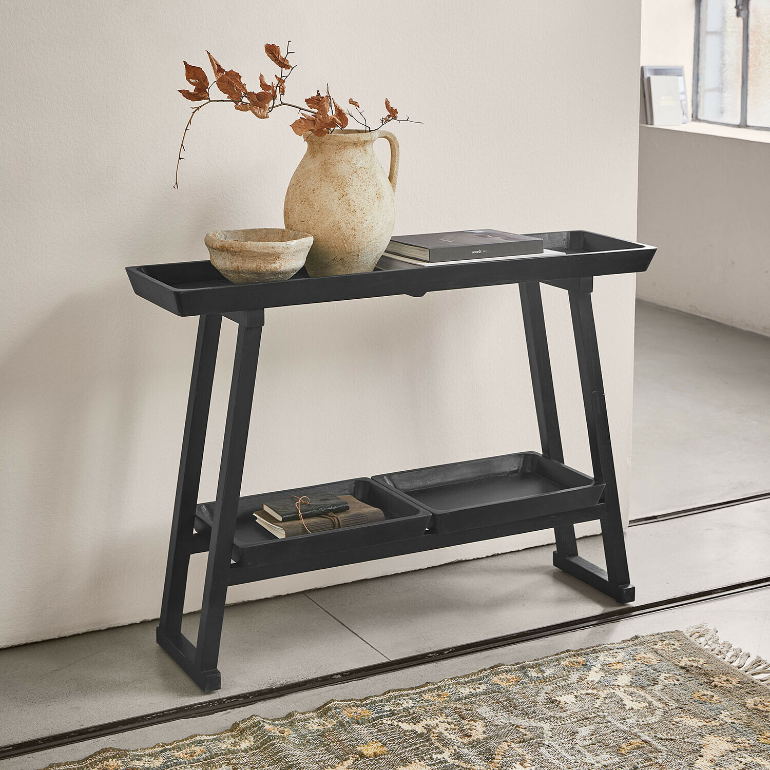 Konsola Ivywood Czarny drewniany stolik z półkami z ceramiczną wazą i książkami w minimalistycznym wnętrzu