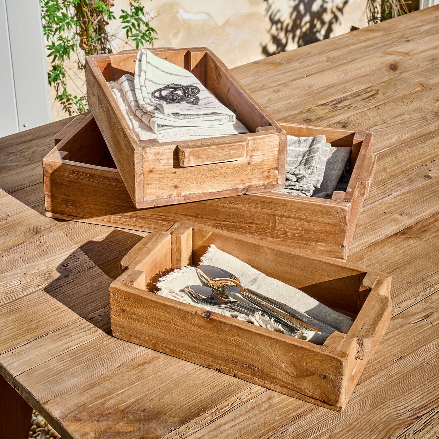 Zestaw trzech drewnianych tac z uchwytami, naturalny kolor, na stole z drewnianej deski, z serwetkami i sztućcami