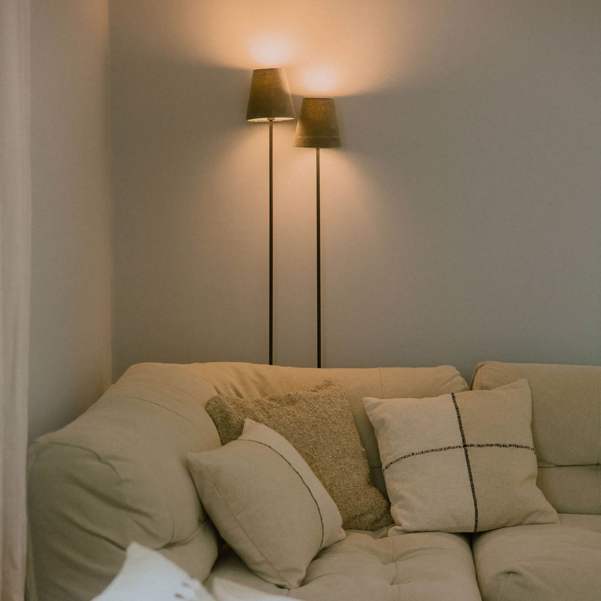 Beżowa sofa z miękkimi poduszkami i dwoma stojącymi lampami z ciemnymi abażurami w salonie