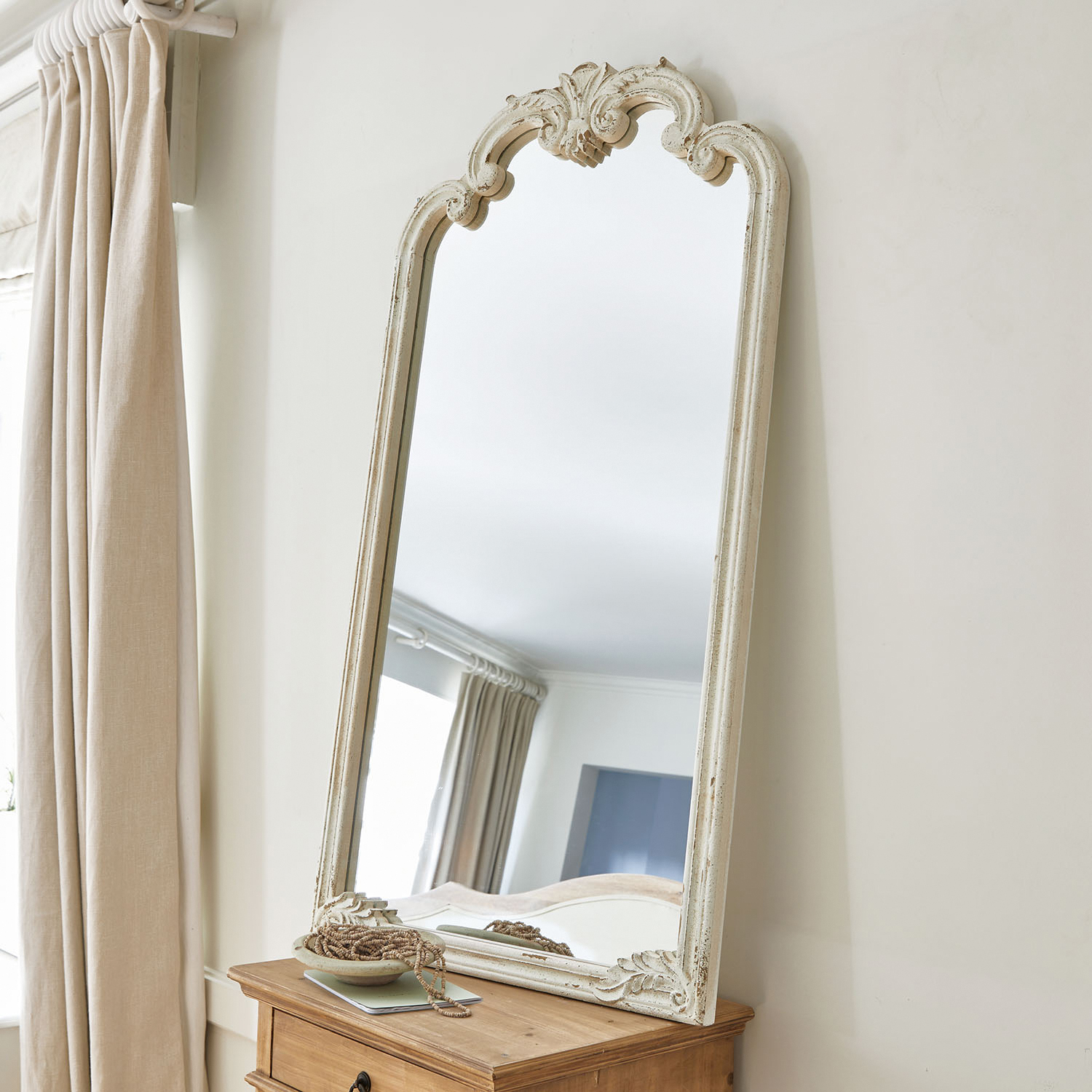 Lustro stojące z białą, postarzaną ramą z drewna o ozdobnym wzorze, dekoracja wnętrza