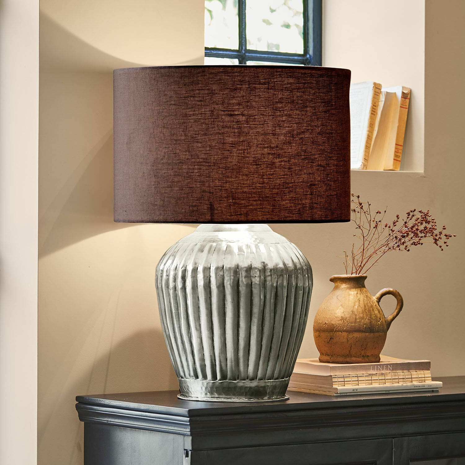Lampa stołowa Fauville Lampka stołowa z metalową, srebrną podstawą i brązowym abażurem na ciemnej komodzie