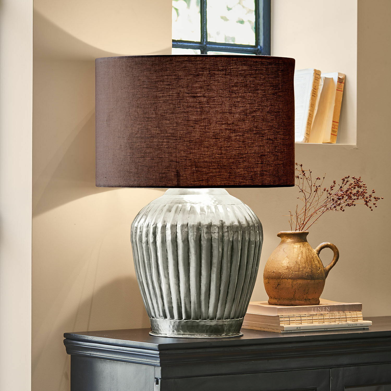 Lampa stołowa Fauville Lampka stołowa z metalową, srebrną podstawą i brązowym abażurem na ciemnej komodzie
