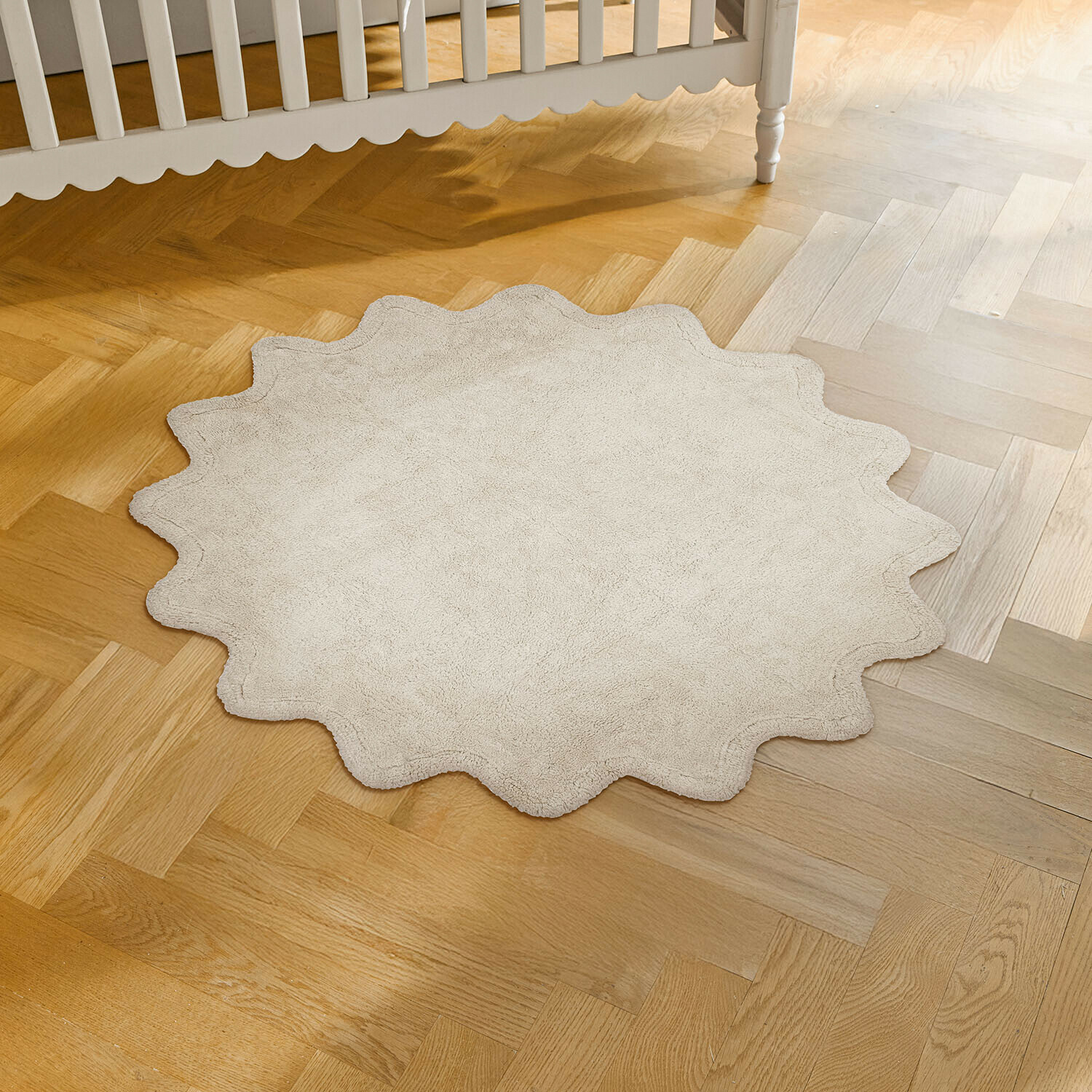 Dywan Wonderfluff Okrągły dywanik z miękkiego beżowego materiału o falistym brzegu na drewnianej podłodze