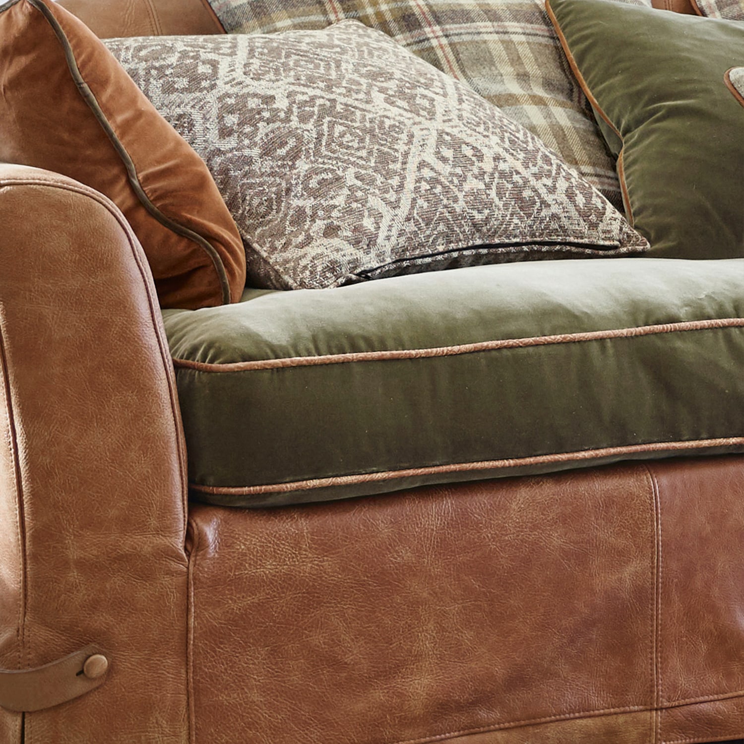 Brązowa skórzana sofa z zielonym welurowym siedziskiem i dekoracyjnymi poduszkami w stylu rustykalnym