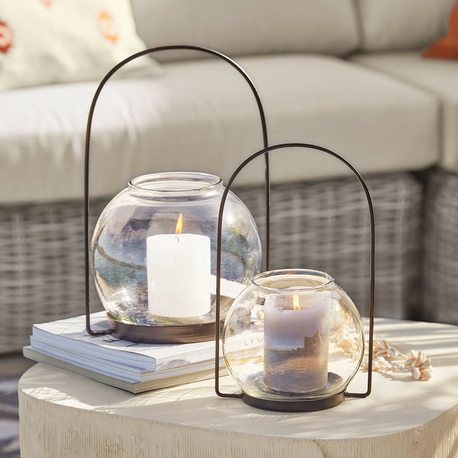 Dwa szklane lampiony z metalowymi uchwytami i palącymi się świecami na jasnym stole dekoracyjnym