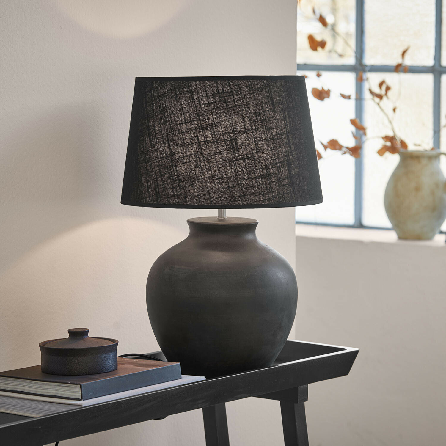 Lampa stołowa Branver Czarna ceramiczna lampa stołowa z tekstylnym abażurem na stoliku z książkami i dekoracją