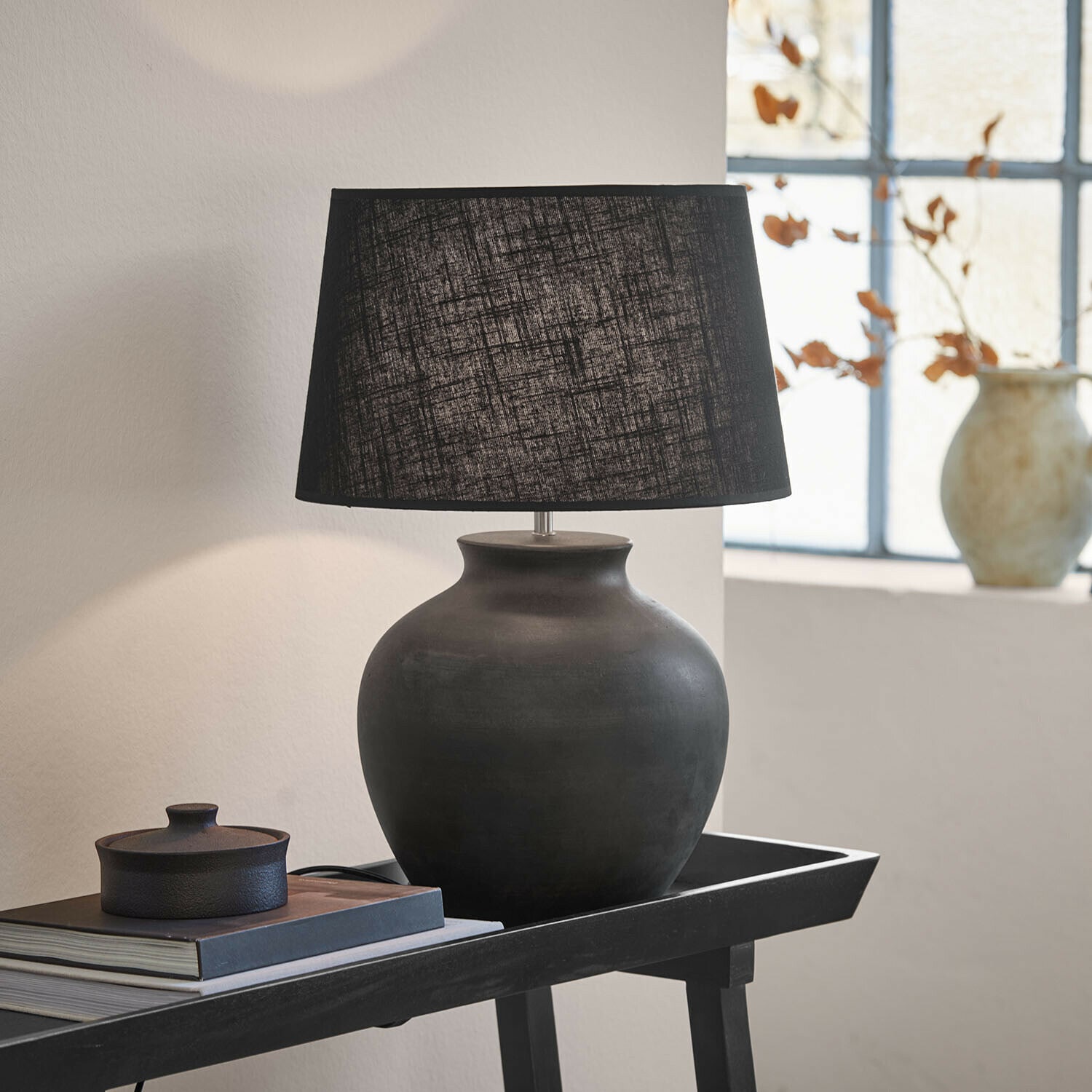 Lampa stołowa Branver Czarna ceramiczna lampa stołowa z tekstylnym abażurem na stoliku z książkami i dekoracją