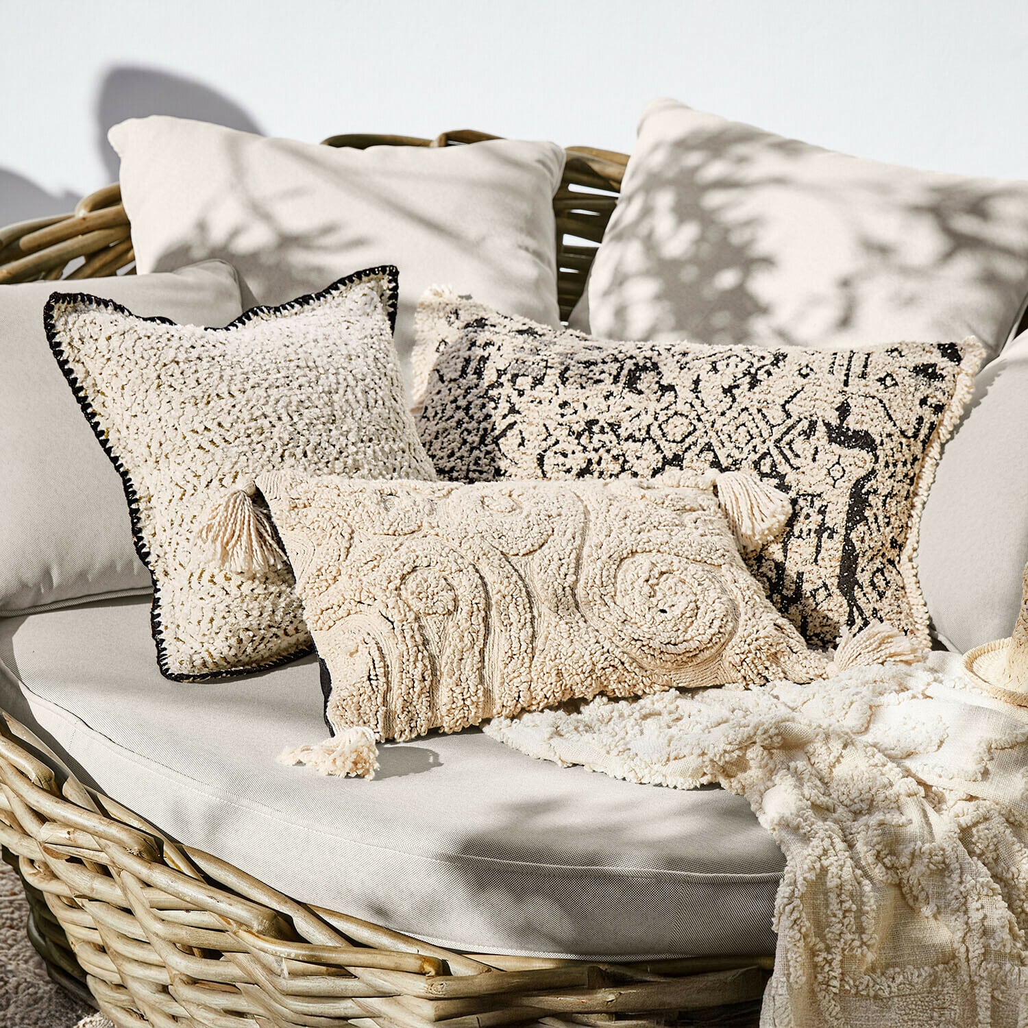 Zestaw kremowych poduszek dekoracyjnych z miękkiego materiału na wiklinowej sofie, styl boho
