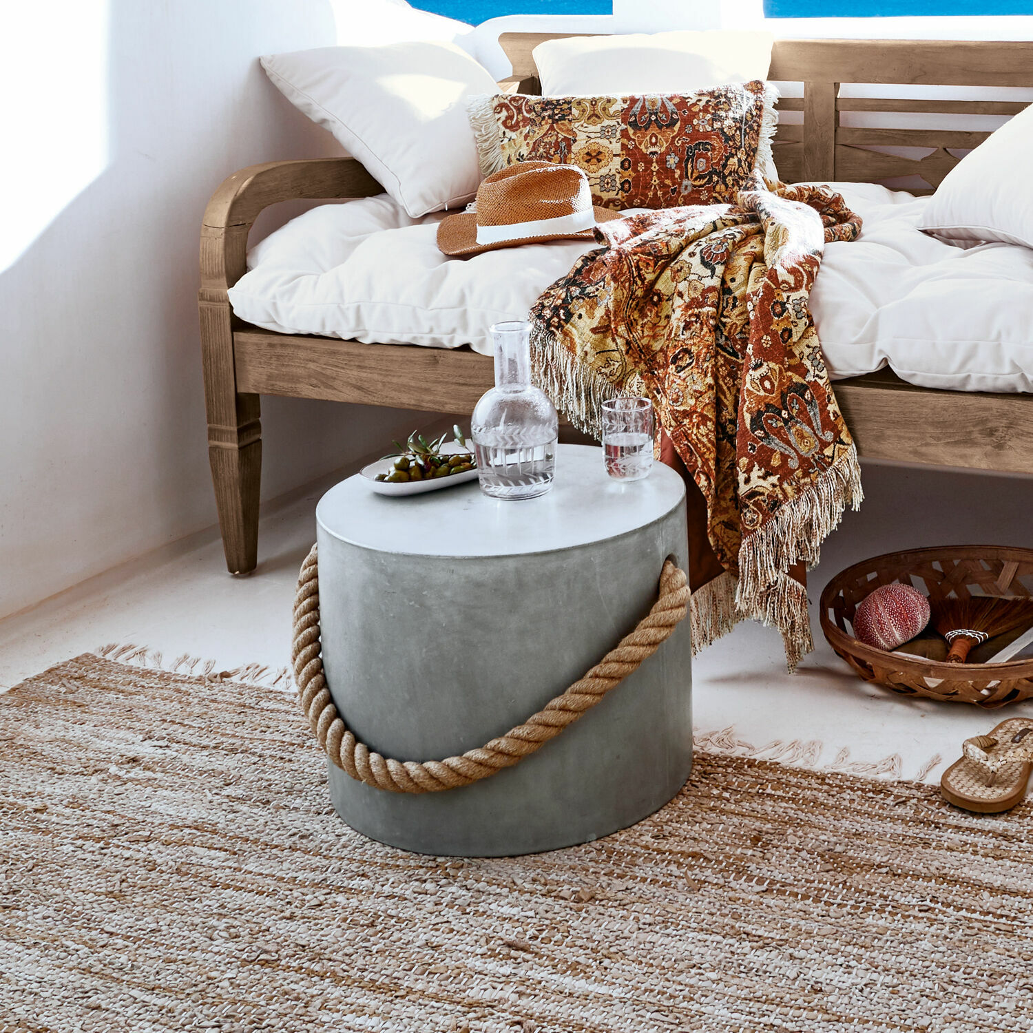 Okrągły stolik z betonu z uchwytem ze sznurka w naturalnym salonie z drewnianą sofą i dekoracyjnym pledem