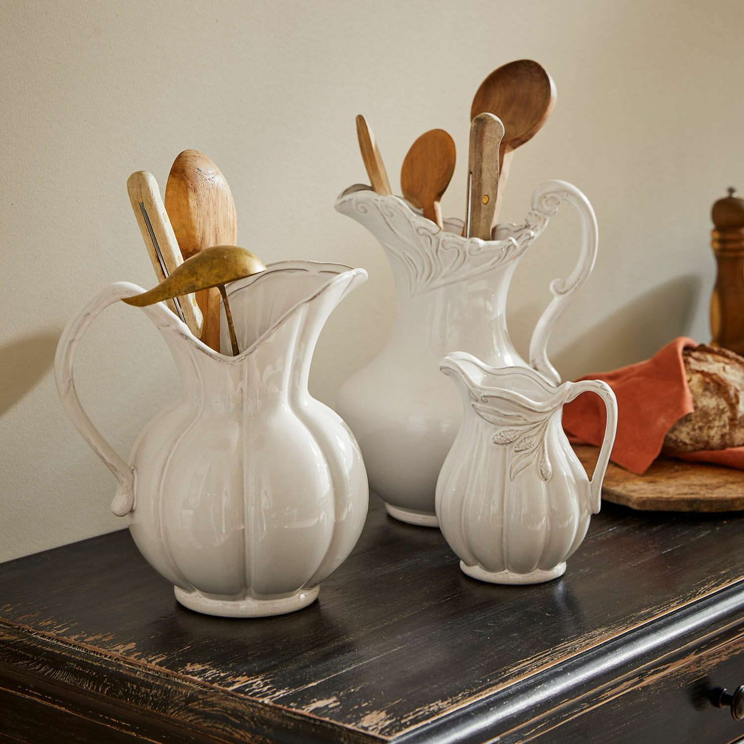 Trzy białe ceramiczne dzbanki na ciemnym drewnianym blacie z drewnianymi łyżkami i chlebem