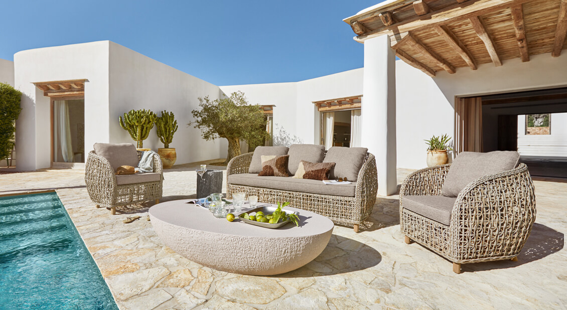 Zestaw mebli ogrodowych z beżowego rattanu z szarymi poduszkami przy basenie na kamiennym tarasie