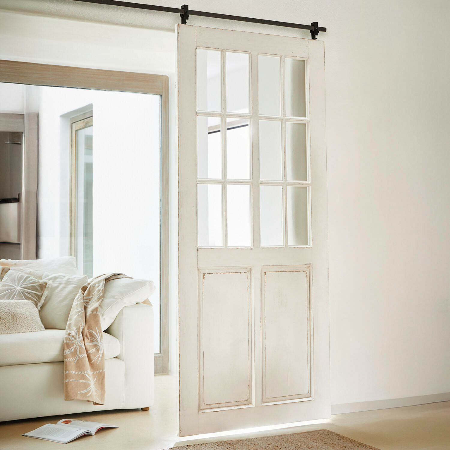 Białe drewniane drzwi przesuwne z przeszklonymi panelami w jasnym, nowoczesnym wnętrzu salonu