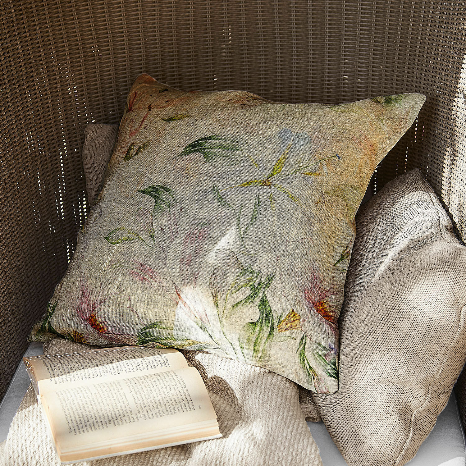Poduszka dekoracyjna z lnu w kwiatowy wzór w naturalnych kolorach na fotelu z wikliny