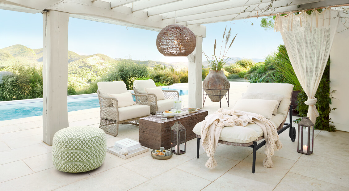 Biały zestaw mebli ogrodowych z poduszkami pod pergolą przy basenie, naturalne dekoracje i lampiony