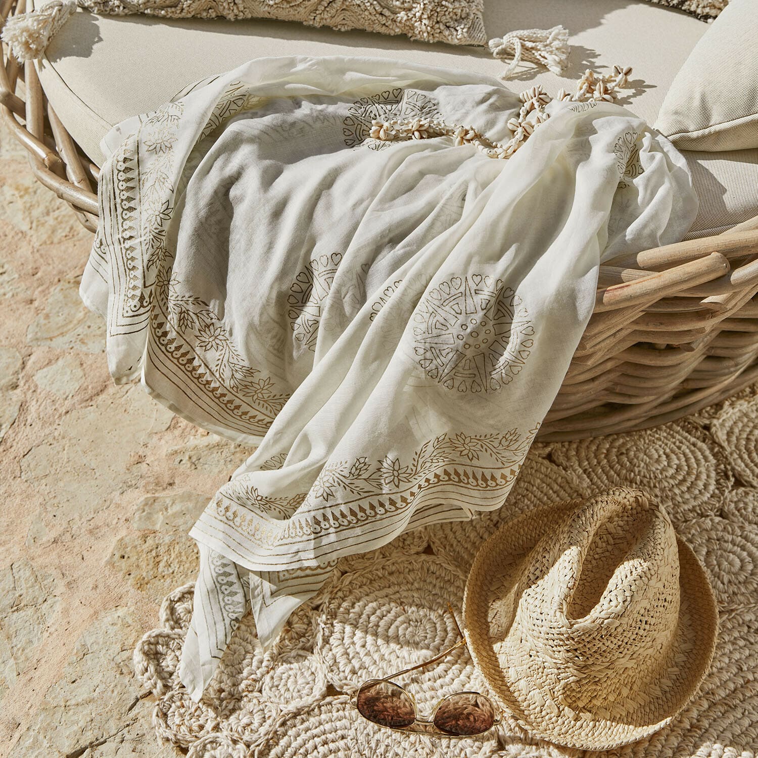 Szal Lamérise Lekki biały szal z delikatnym wzorem leżący na wiklinowym fotelu obok słomkowego kapelusza i okularów przeciwsłonecznych