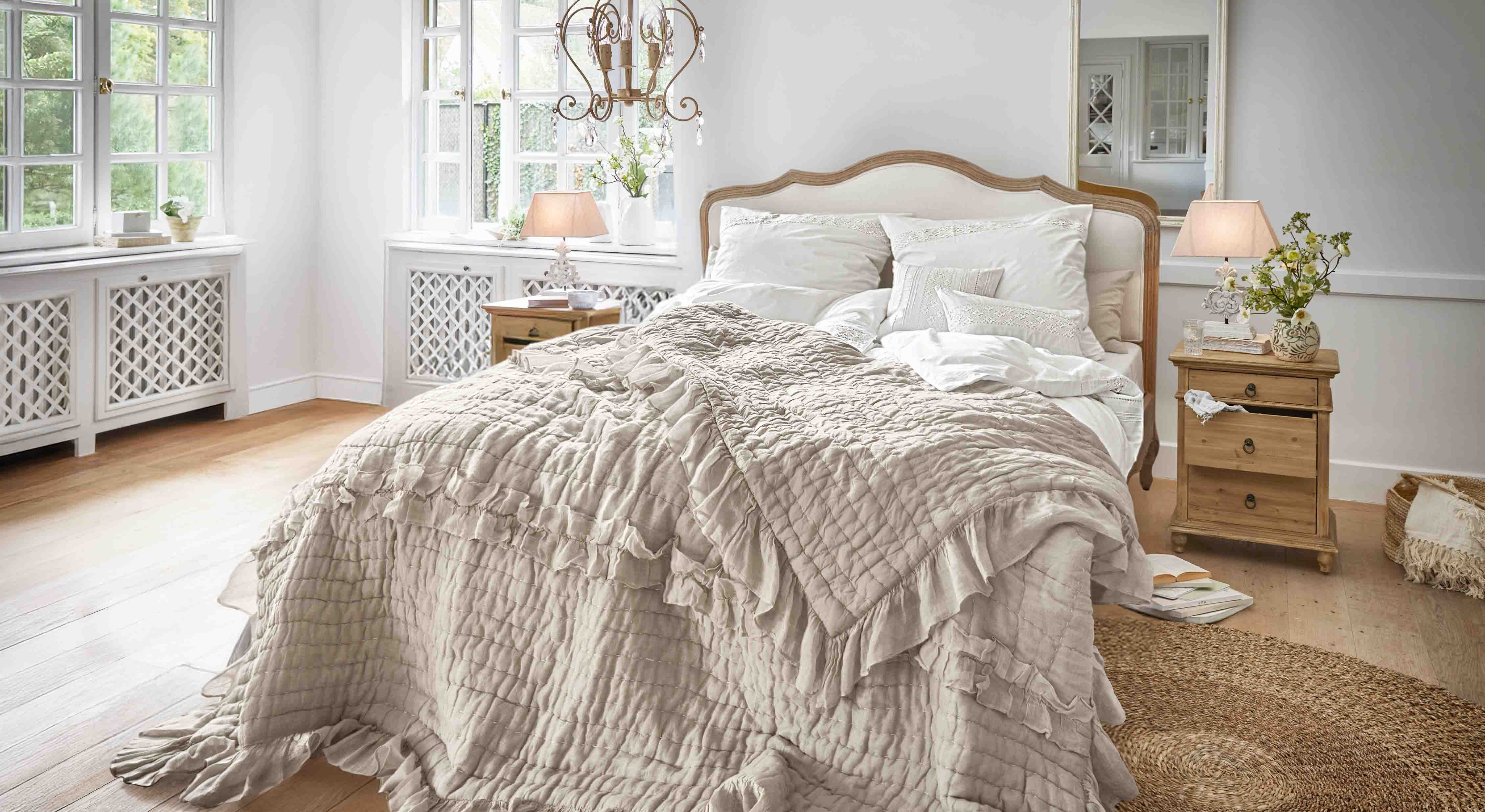 Przytulna sypialnia z łóżkiem w beżowej narzucie z falbanami i drewnianymi stolikami nocnymi