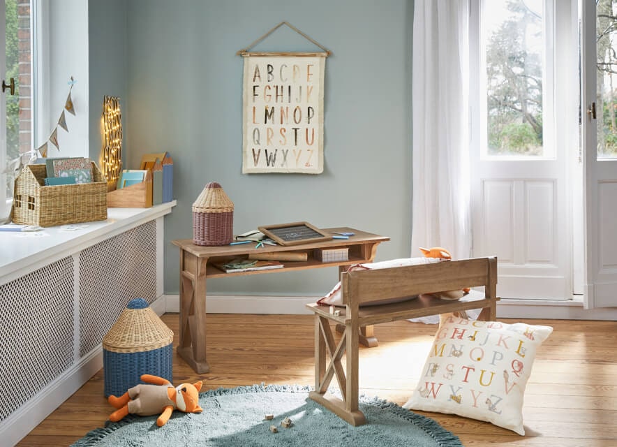 Drewniane biurko i ławka w pokoju dziecięcym z dekoracjami alfabetu i wiklinowymi koszami