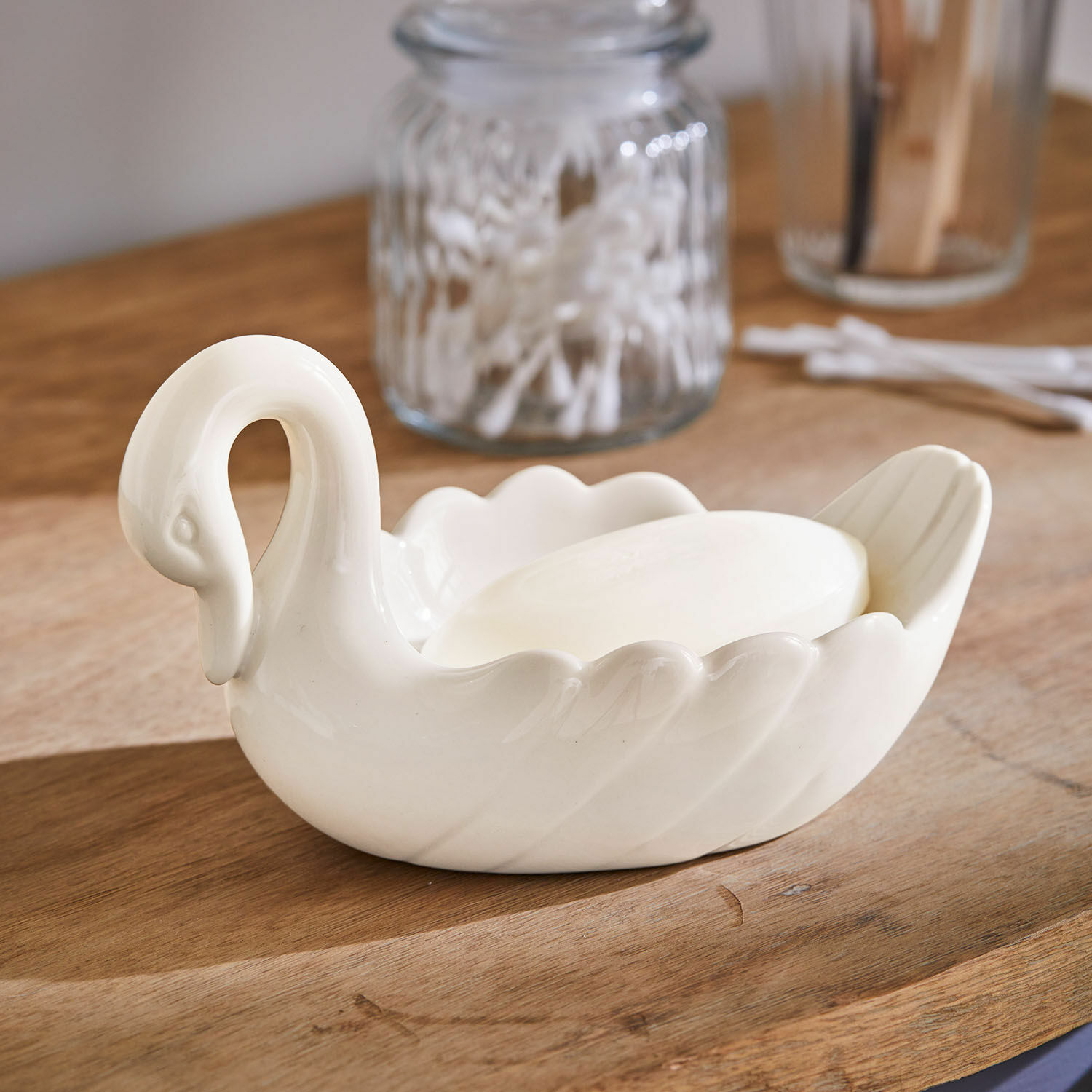 Mydelniczka Casavela Biała ceramiczna mydelniczka w kształcie łabędzia z mydłem na drewnianym blacie, akcesoria łazienkowe