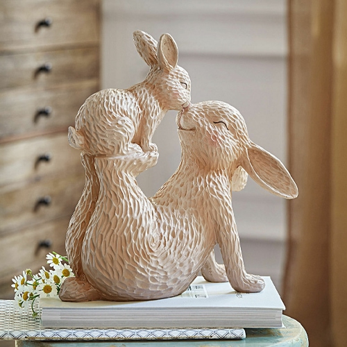 Beżowa ceramiczna figurka dwóch królików w przytulnej pozie na stole z książkami, dekoracja wiosenna
