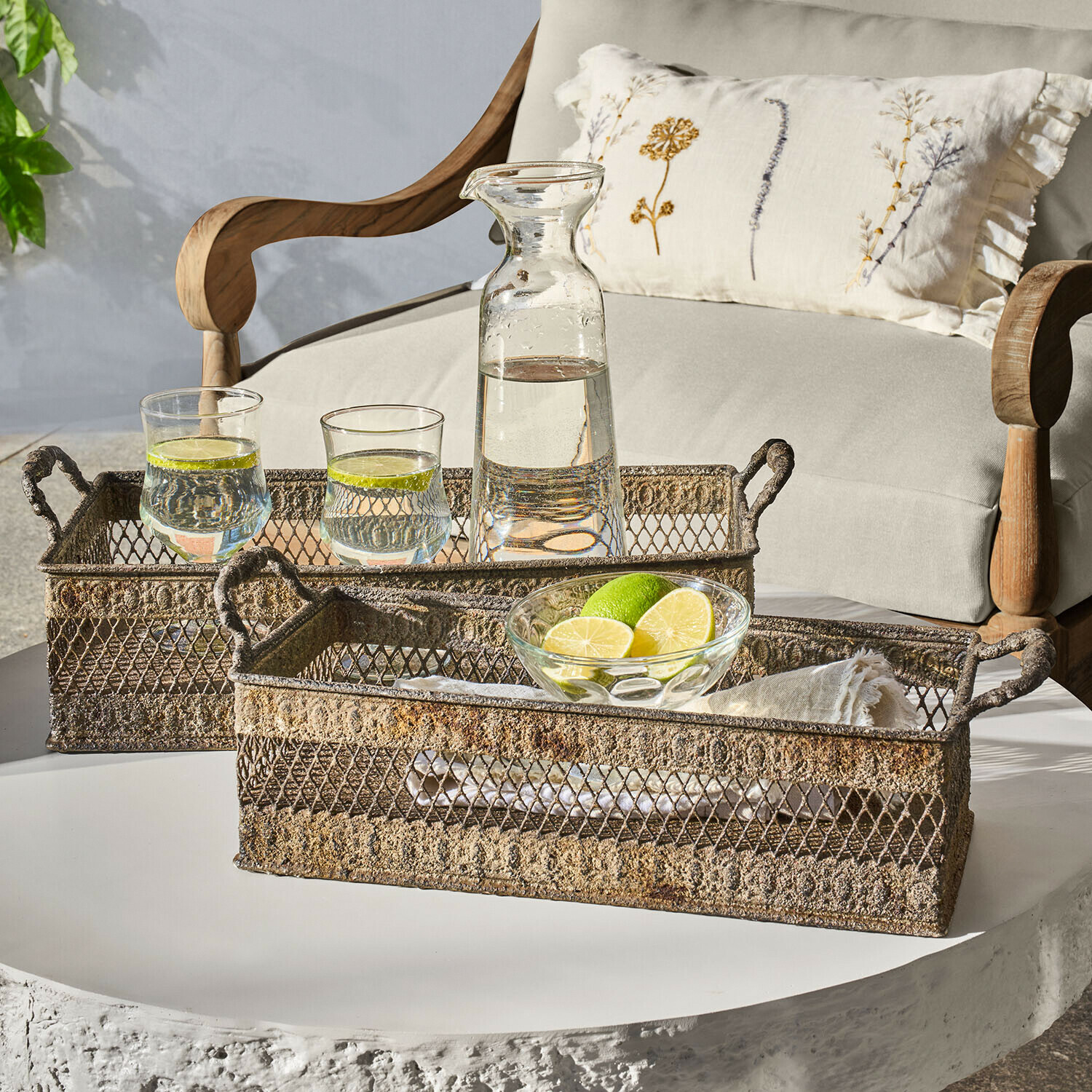 Dwa rustykalne metalowe tace z uchwytami na białym stole z karafką i szklankami z wodą i limonką