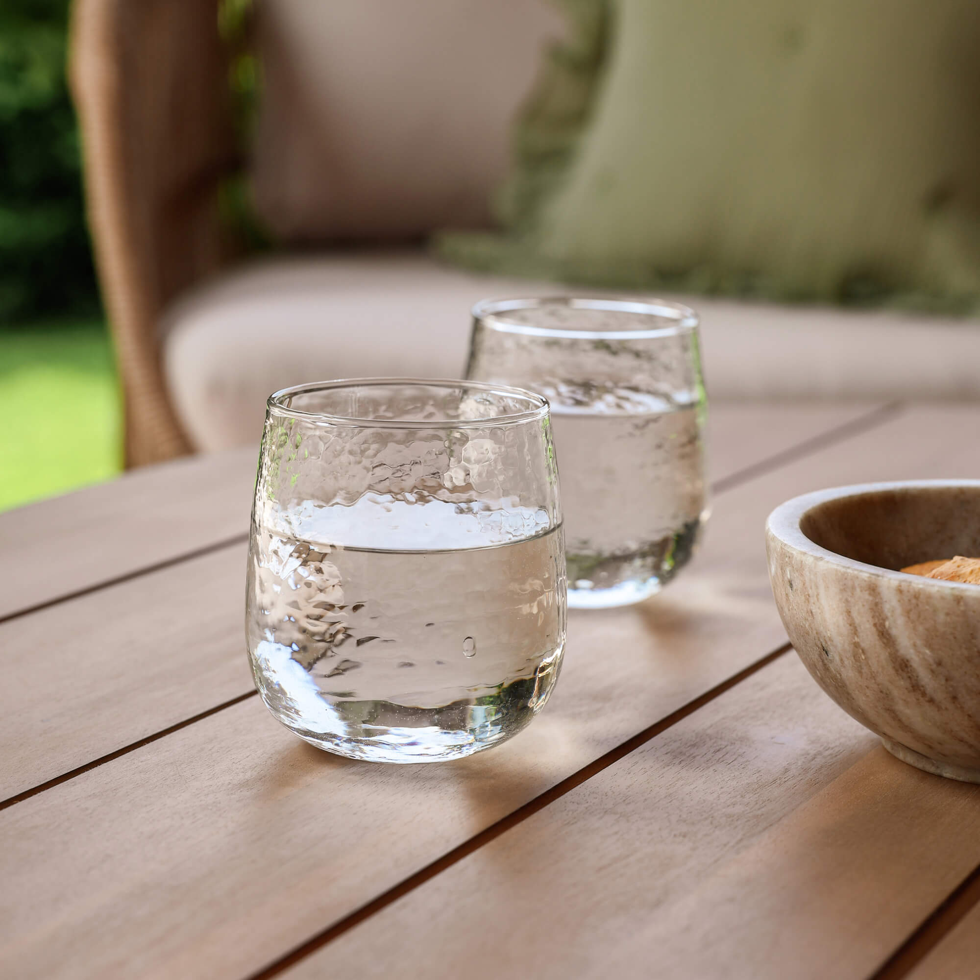 Dwa przezroczyste szklanki z wodą na drewnianym stole w ogrodzie z miską z kamienia