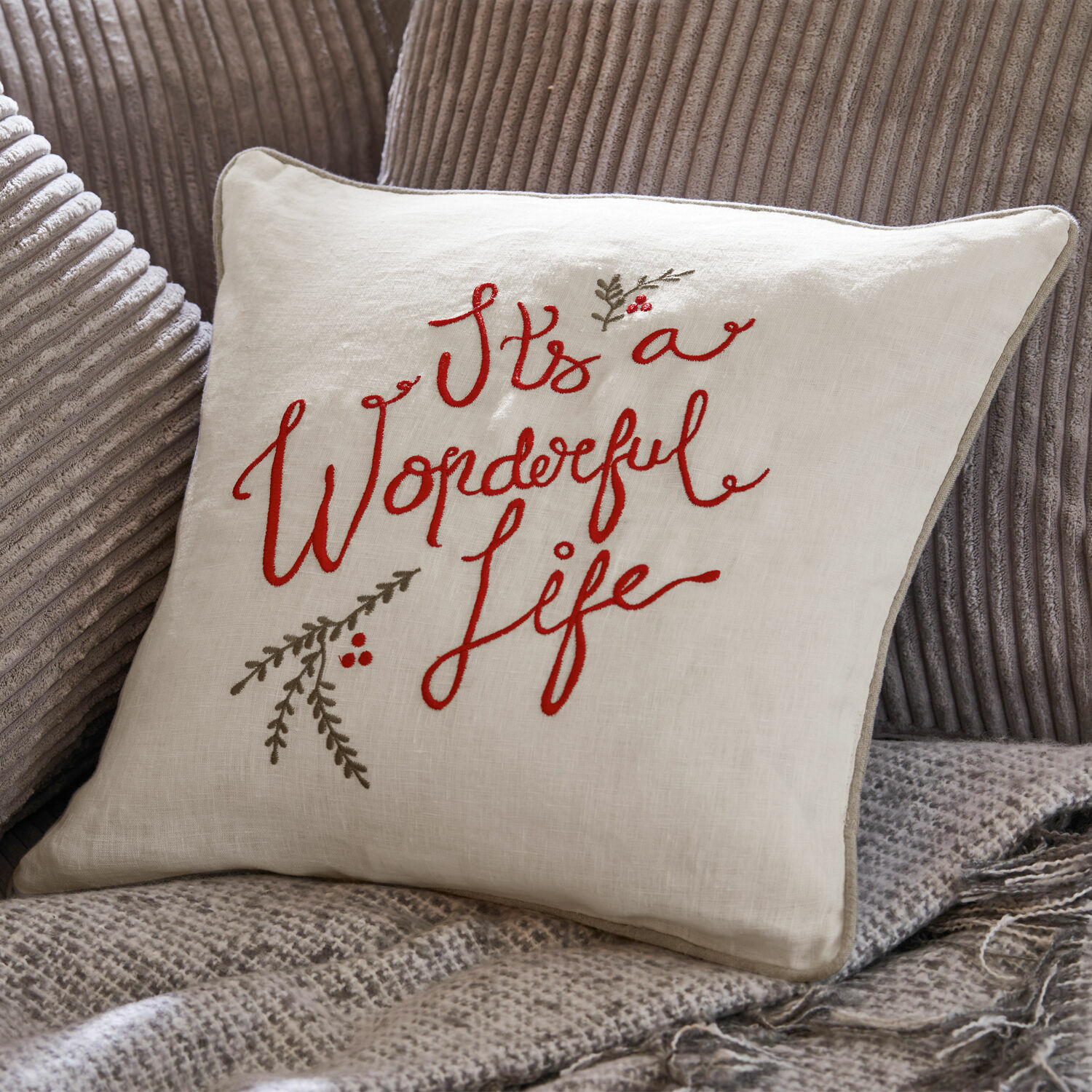 Poszewka na poduszkę Wonderful Beżowa lniana poduszka z czerwonym haftem "It's a Wonderful Life" na szarym tle z tkaniny.