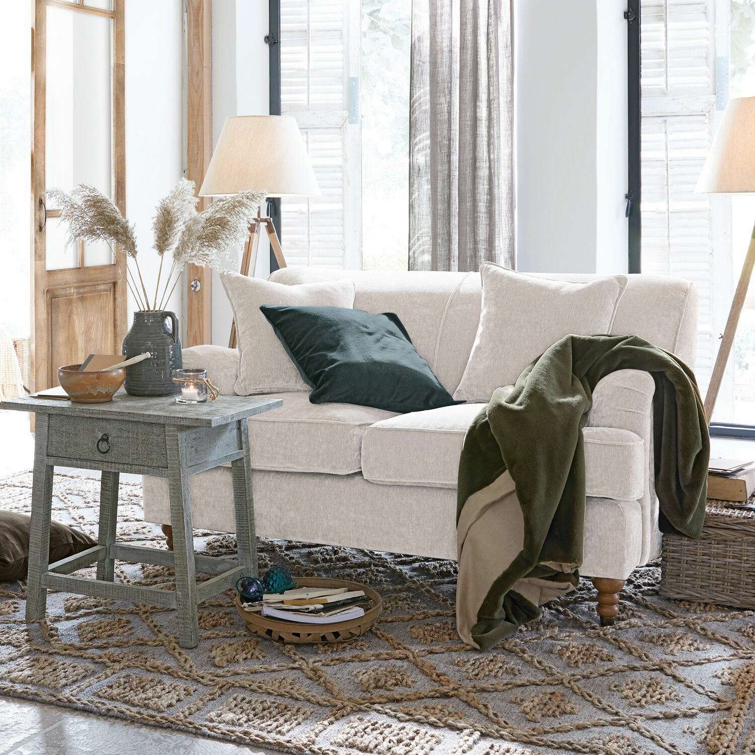 Beżowa sofa z miękkiego materiału z zielonym kocem i poduszką w przytulnym salonie z drewnianym stolikiem