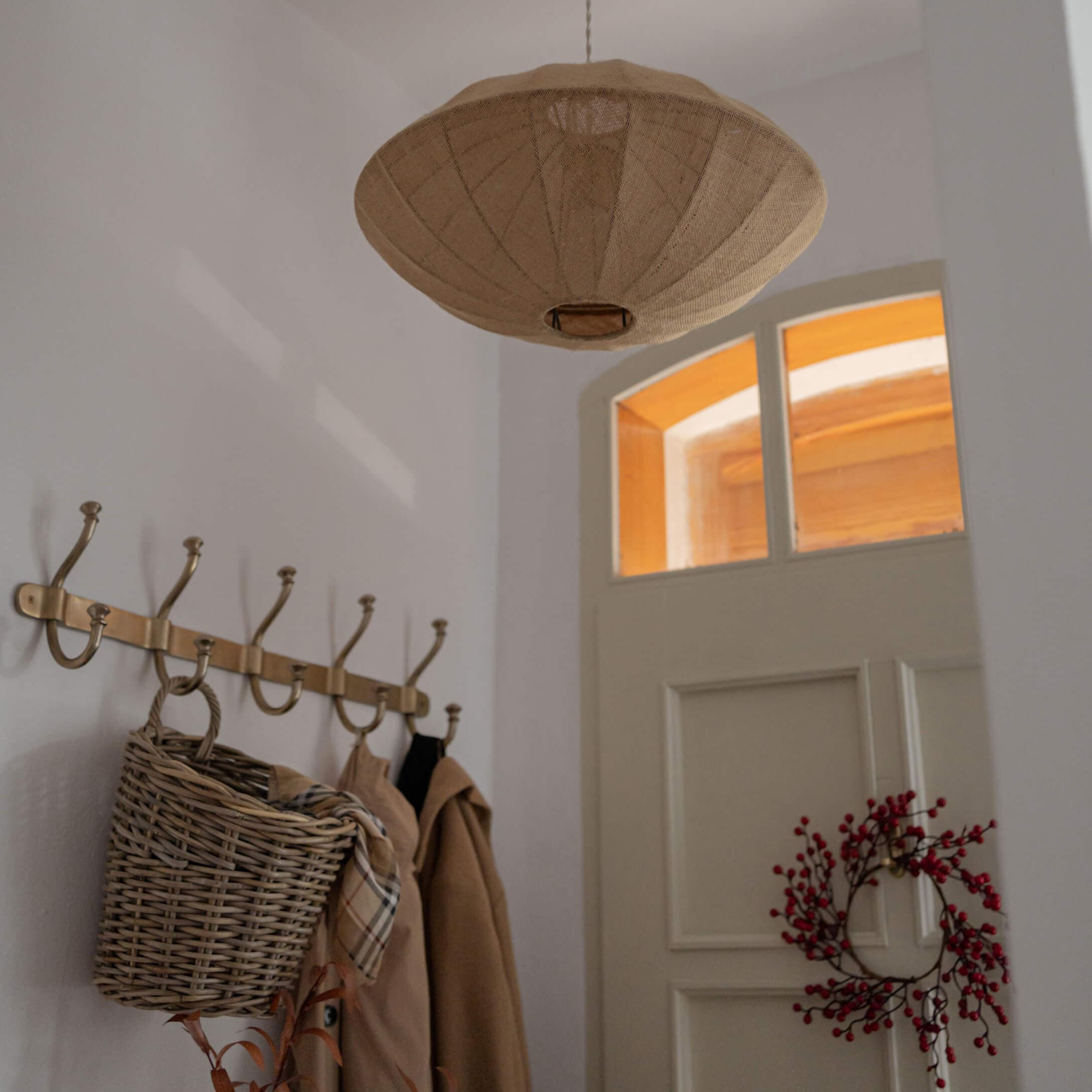 Beżowa lampa wisząca z tkaniny w kształcie rozłożystej czaszy w przytulnym wnętrzu z wieszakiem i wiklinowym koszem