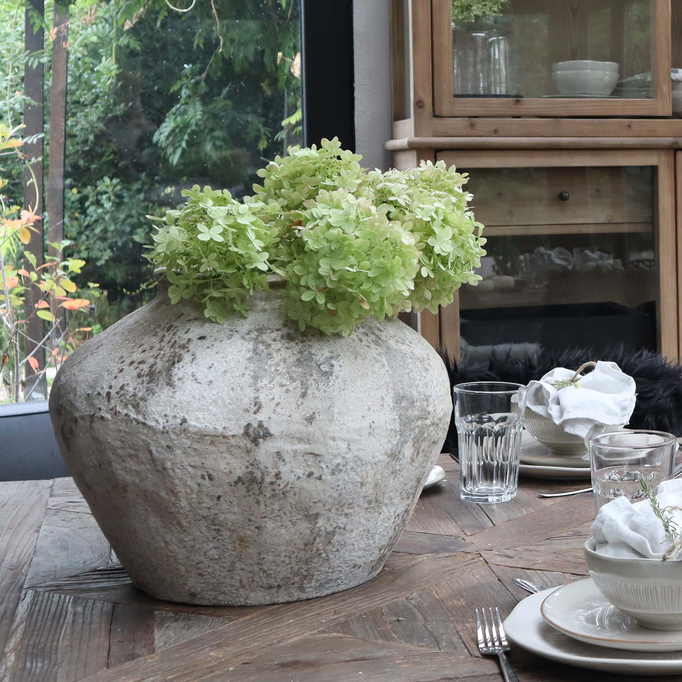 Duży ceramiczny wazon w kolorze szarym z zielonymi kwiatami na drewnianym stole w jadalni