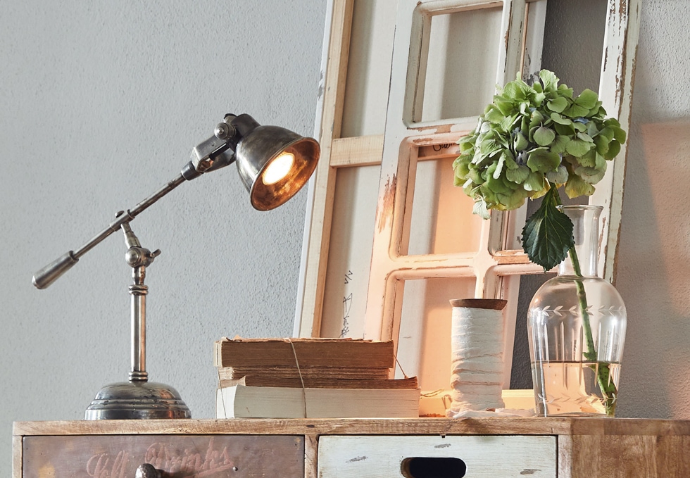 Metalowa lampa stołowa w stylu industrialnym na drewnianym blacie z książkami i wazonem z zielonym kwiatem