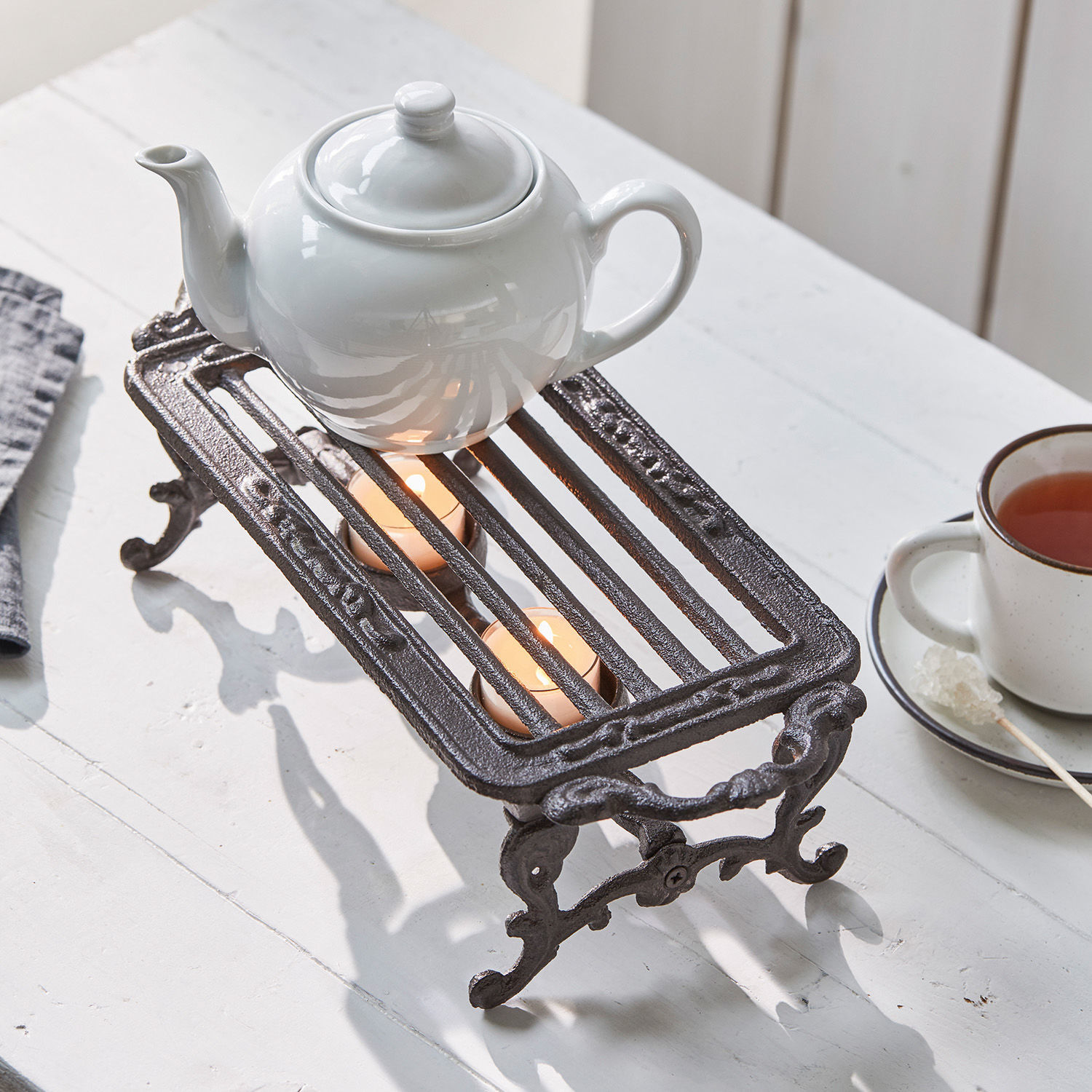 Podgrzewacz Raimond Żeliwny podgrzewacz do dzbanka z dwoma świecami tealight na białym stole do herbaty