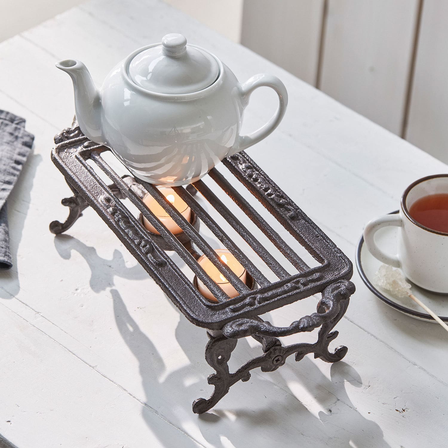 Podgrzewacz Raimond Żeliwny podgrzewacz do dzbanka z dwoma świecami tealight na białym stole do herbaty