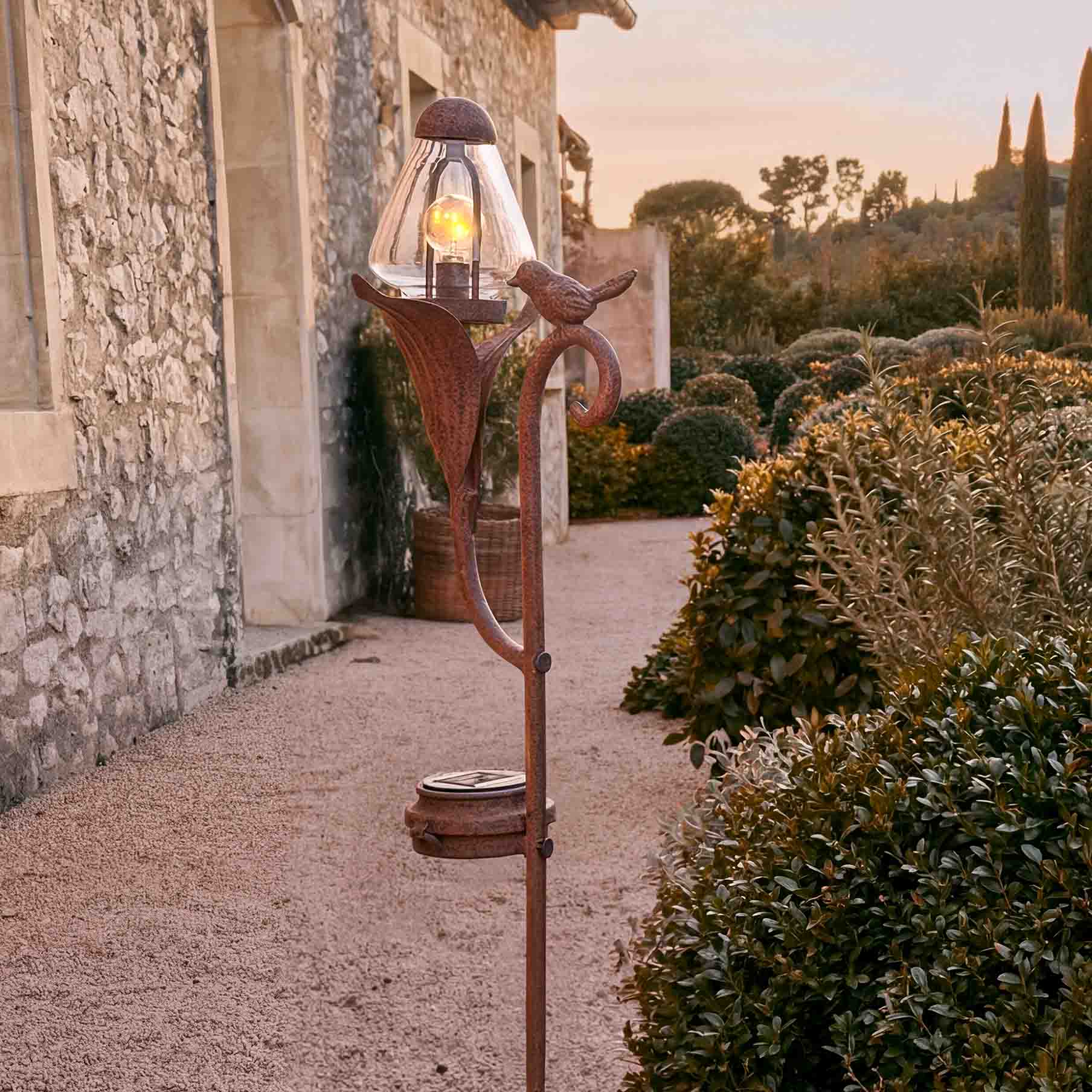 Ozdobna lampa ogrodowa z metalu w kolorze rdzy z kloszem ze szkła i motywem ptaka