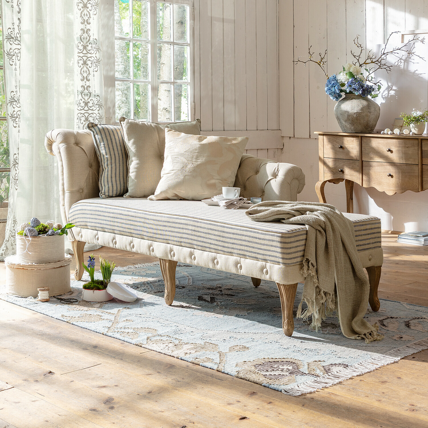 Szezlong Viviani Beżowa pikowana sofa z drewnianymi nogami i pasami na siedzisku w jasnym salonie z dekoracjami