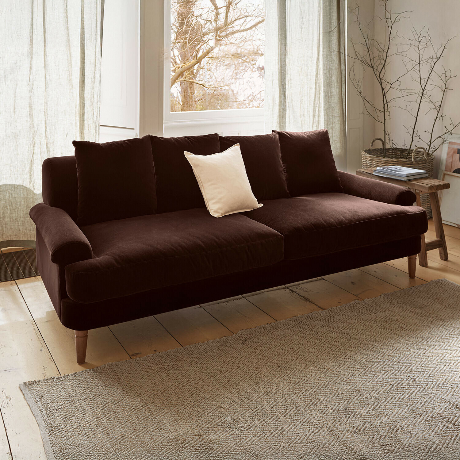 Sofa Rivermere Brązowa welurowa sofa z jasną poduszką w przytulnym salonie z naturalnym światłem