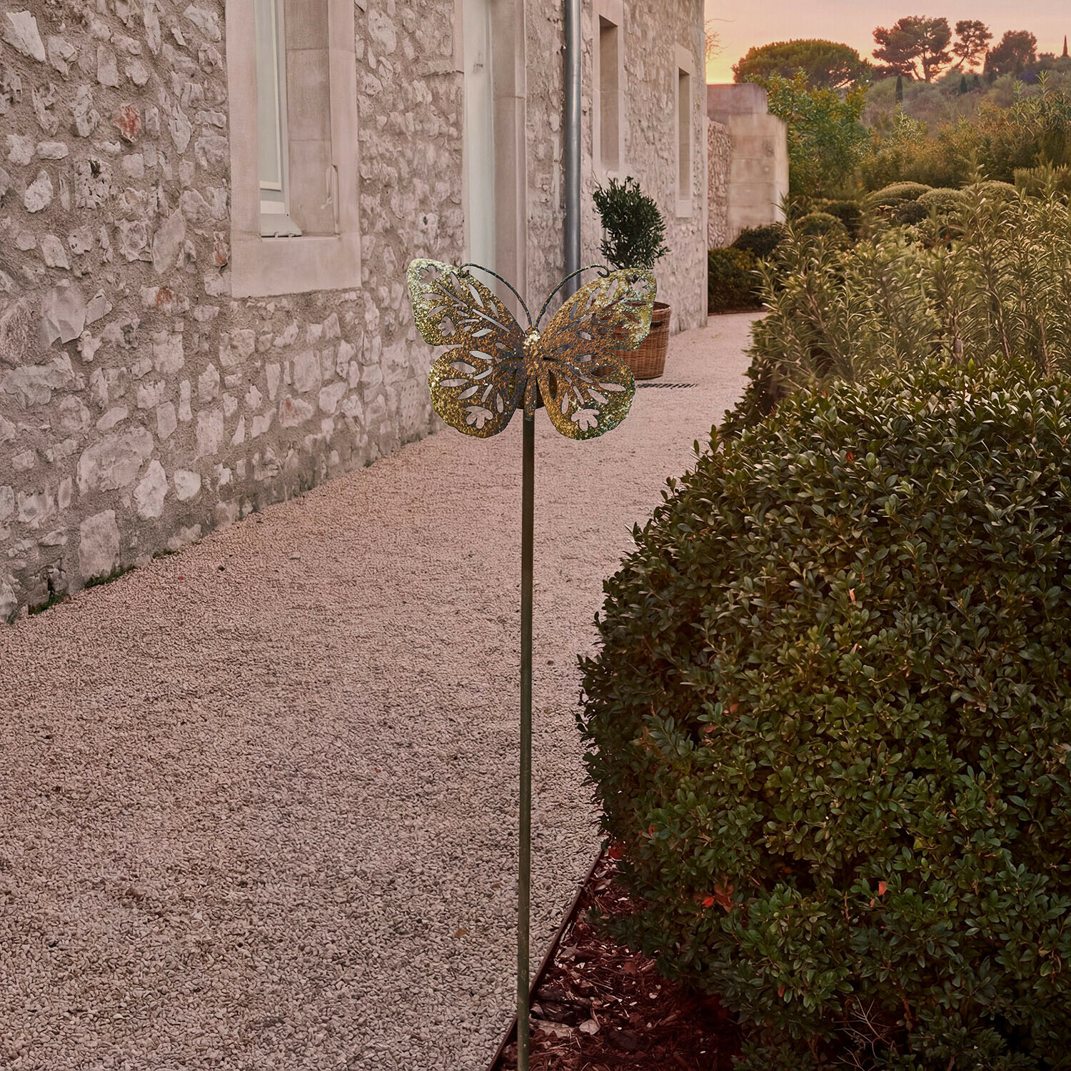 Metalowa dekoracja ogrodowa w kształcie motyla w kolorze mosiądzu na tle kamiennego muru i zieleni