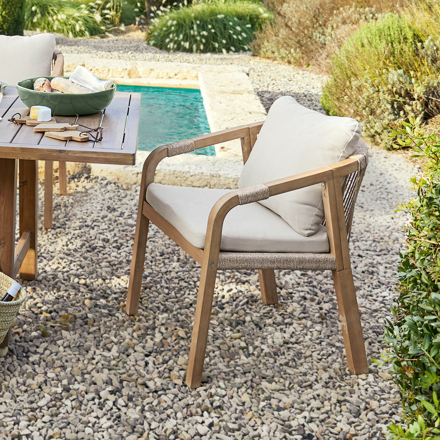 Krzesło ogrodowe z drewna i jasnymi poduszkami na kamiennym patio przy basenie