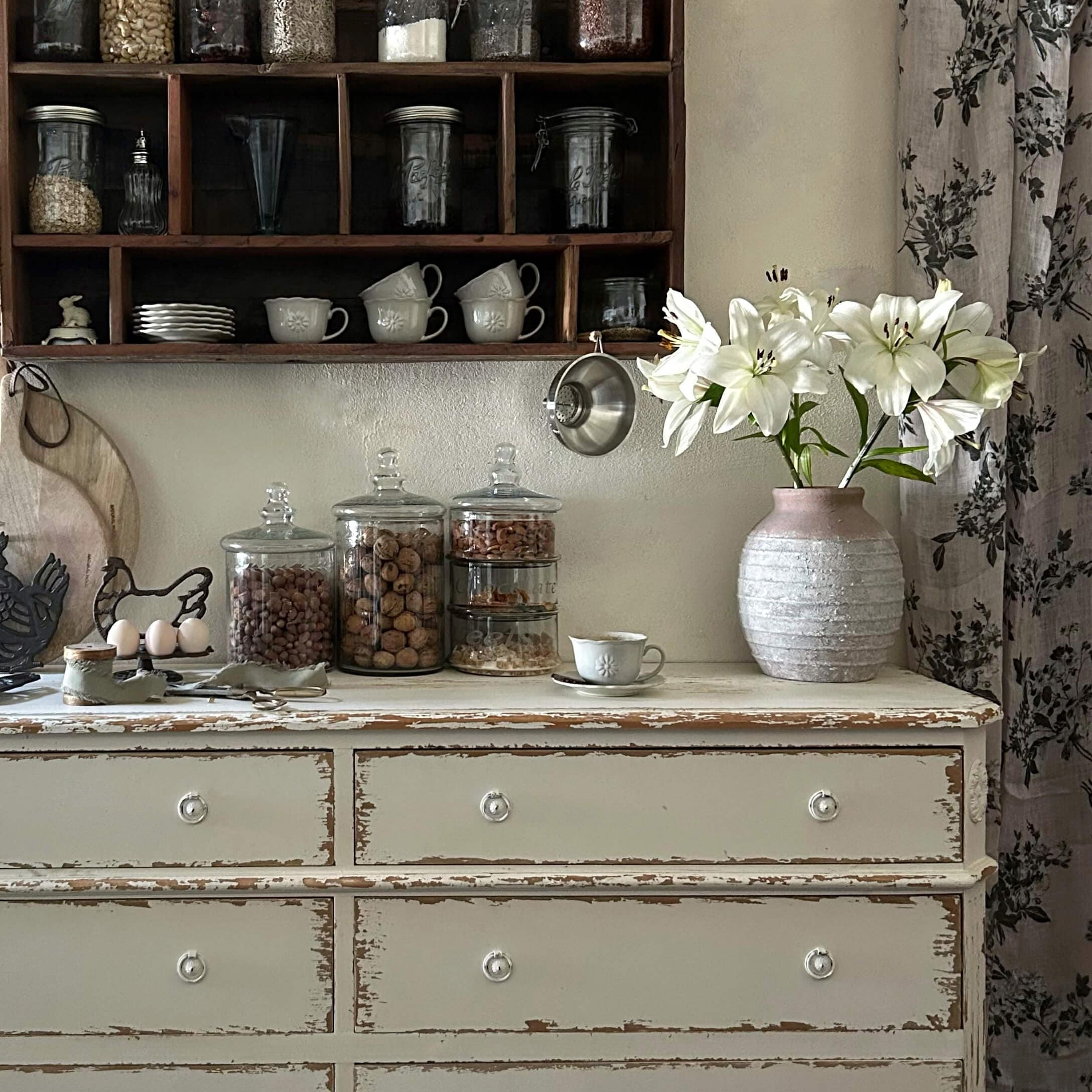 Rustykalna biała komoda z ceramiczną różową wazą i białymi liliami w kuchni vintage