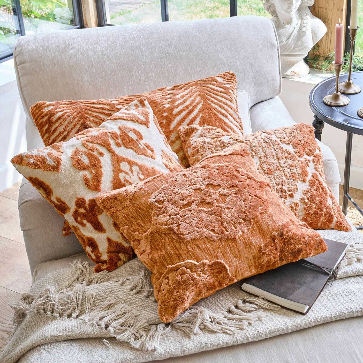 Zestaw poduszek dekoracyjnych w odcieniach pomarańczowego z wzorami na jasnej sofie z kocem