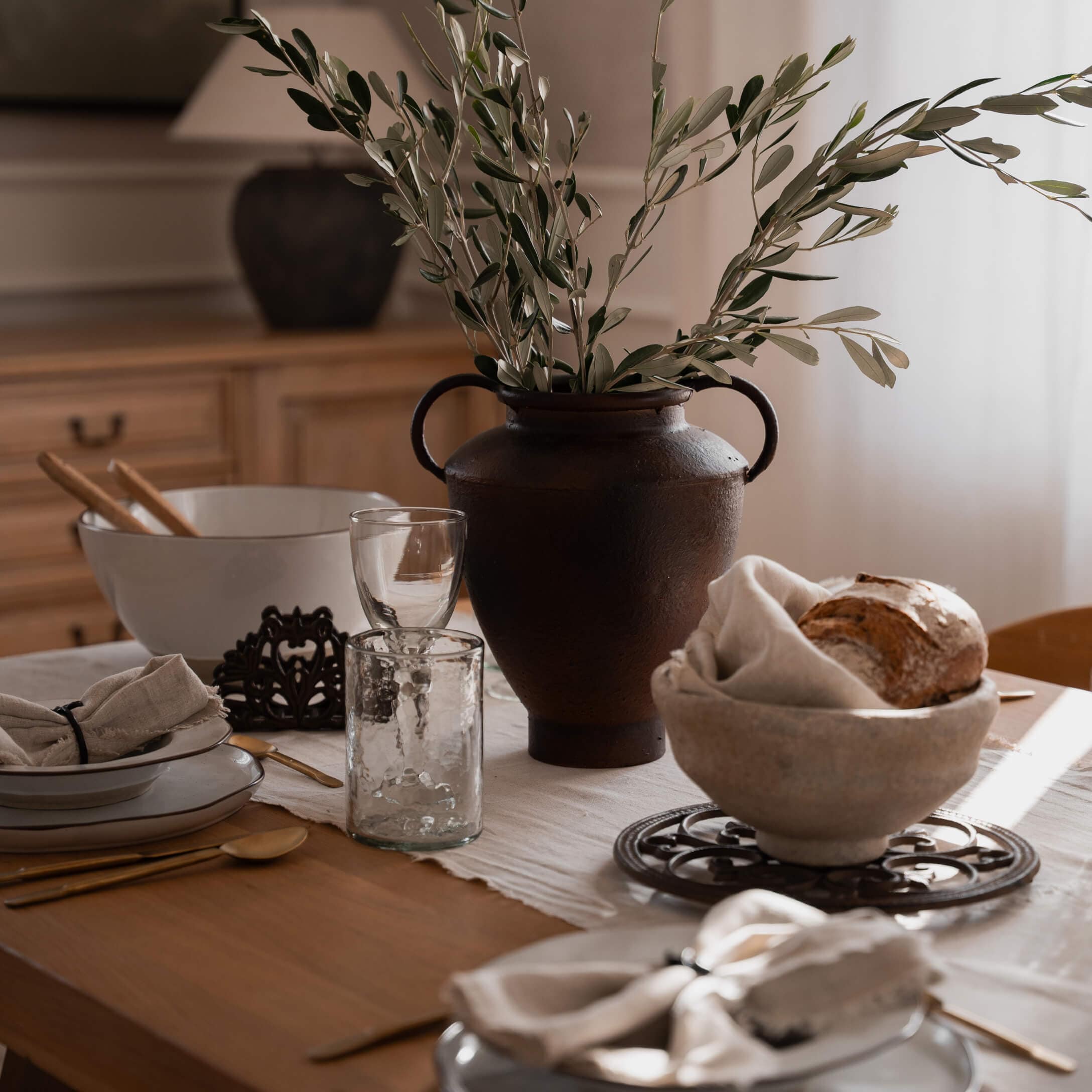 Rustykalny brązowy ceramiczny wazon z zielonymi gałązkami na drewnianym stole z zastawą stołową