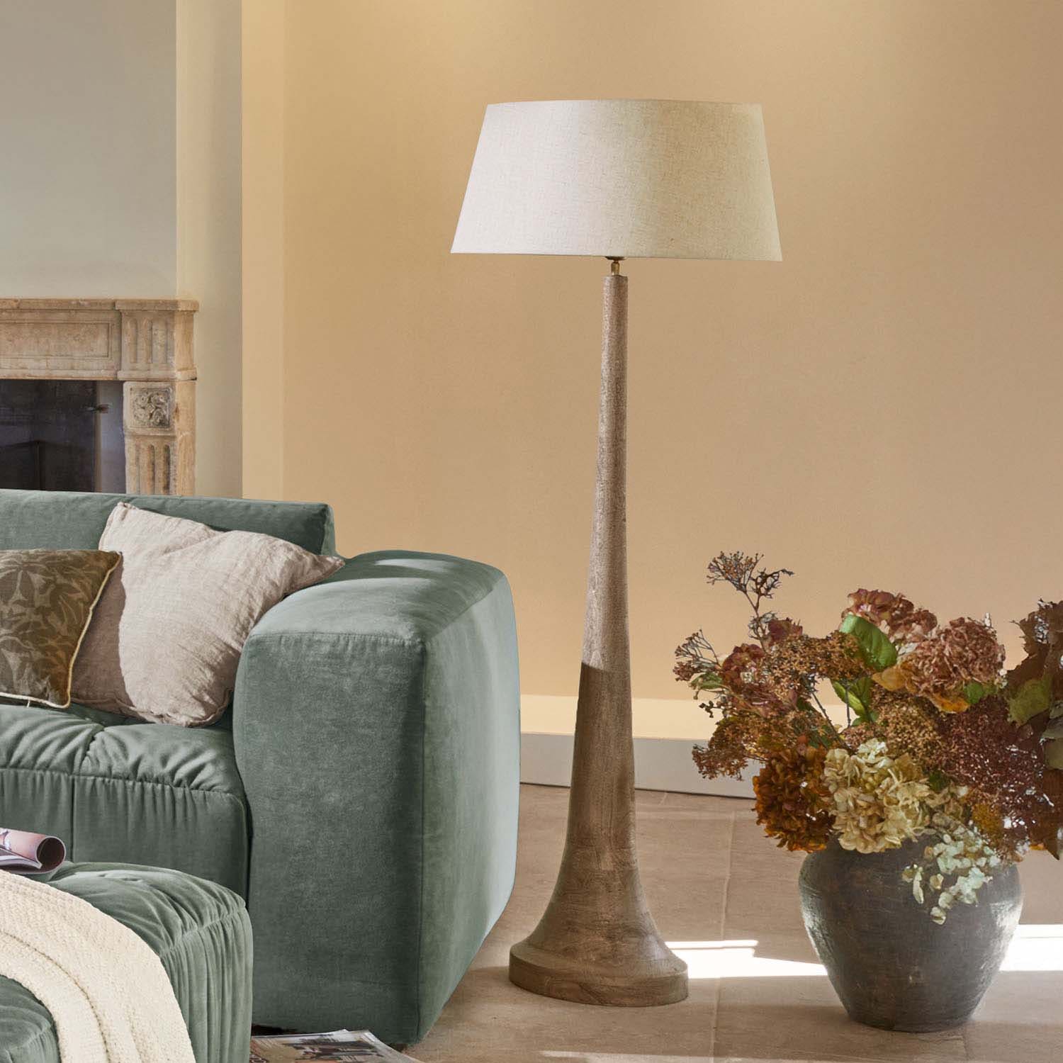 Lampa podłogowa z drewnianą podstawą i beżowym abażurem w nowoczesnym salonie z zieloną sofą