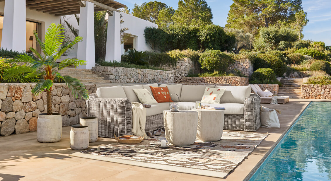 Przytulny narożnik z jasnoszarego rattanu z kremowymi poduszkami przy basenie w stylu śródziemnomorskim