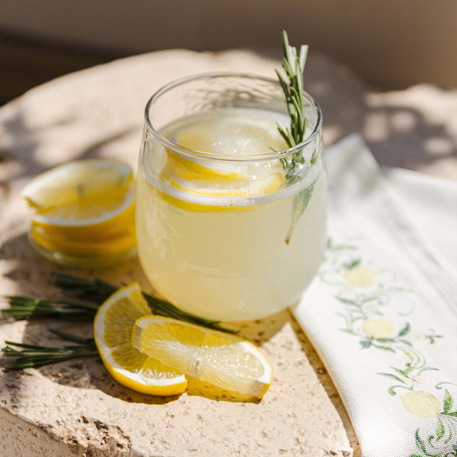 Szklanka lemoniady z plasterkami cytryny i gałązką rozmarynu na kamiennym blacie z serwetką