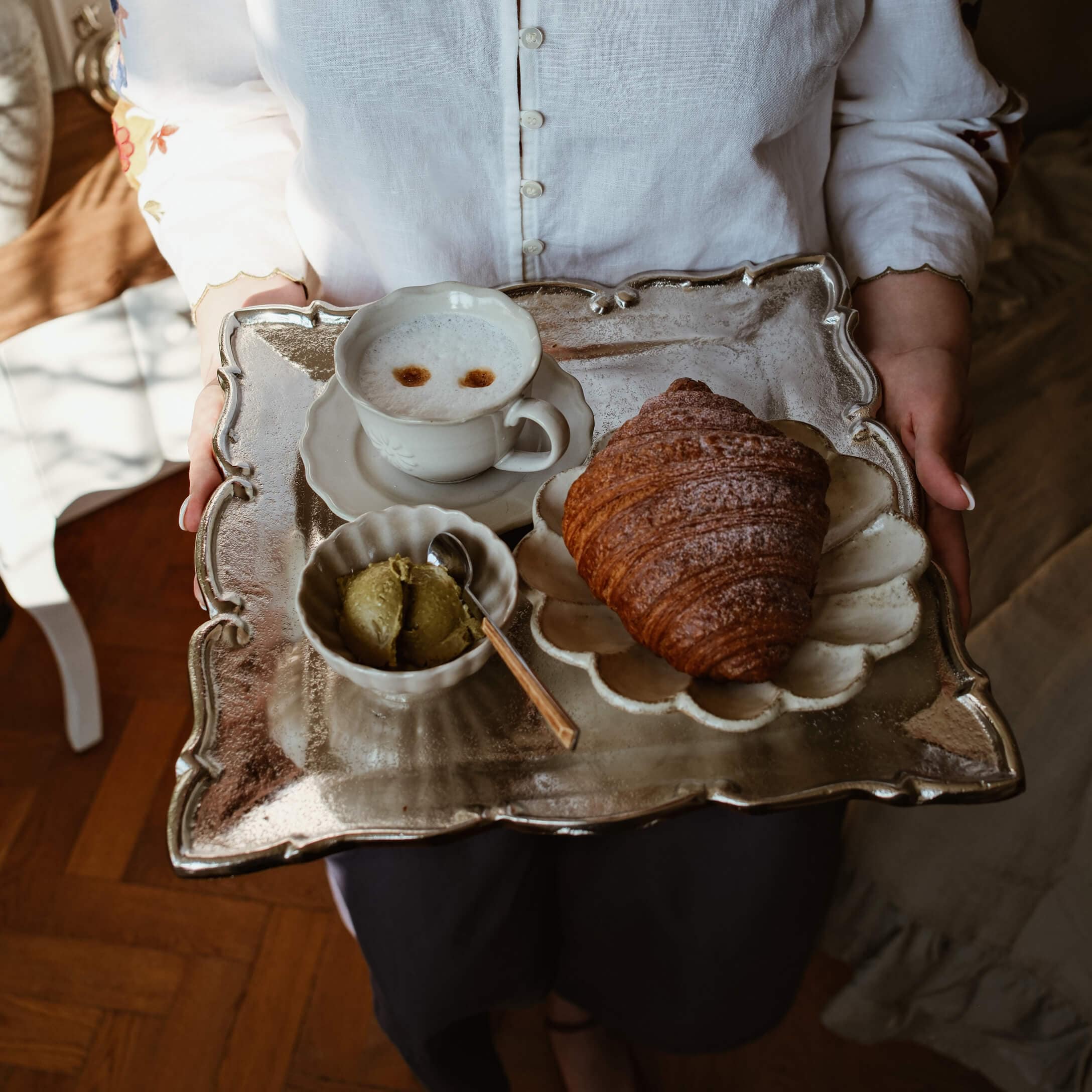 Taca z metalowym wykończeniem z croissantem, filiżanką kawy i zielonym masłem na białej porcelanie