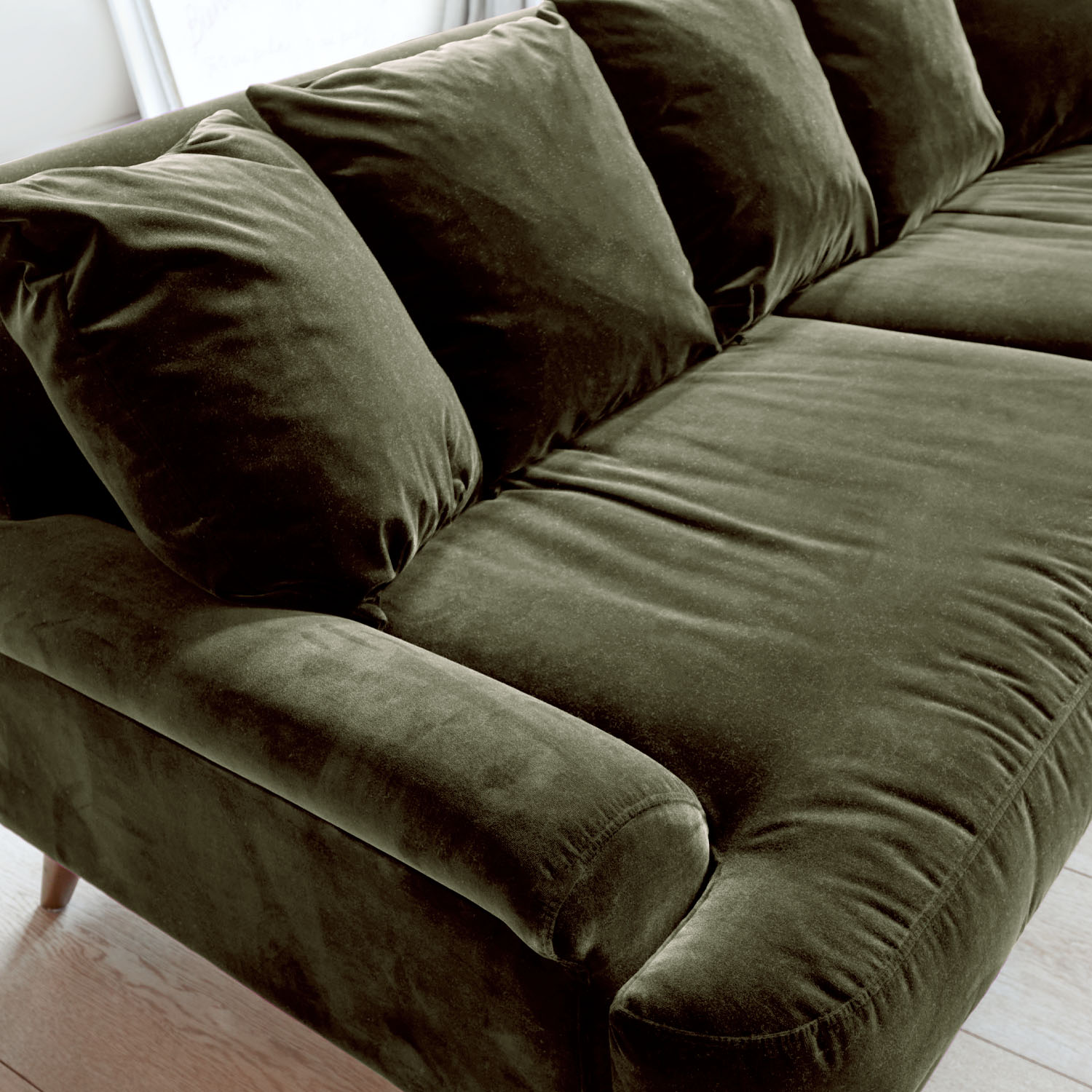 Zielona aksamitna sofa z miękkimi poduszkami i wygodnymi podłokietnikami do salonu