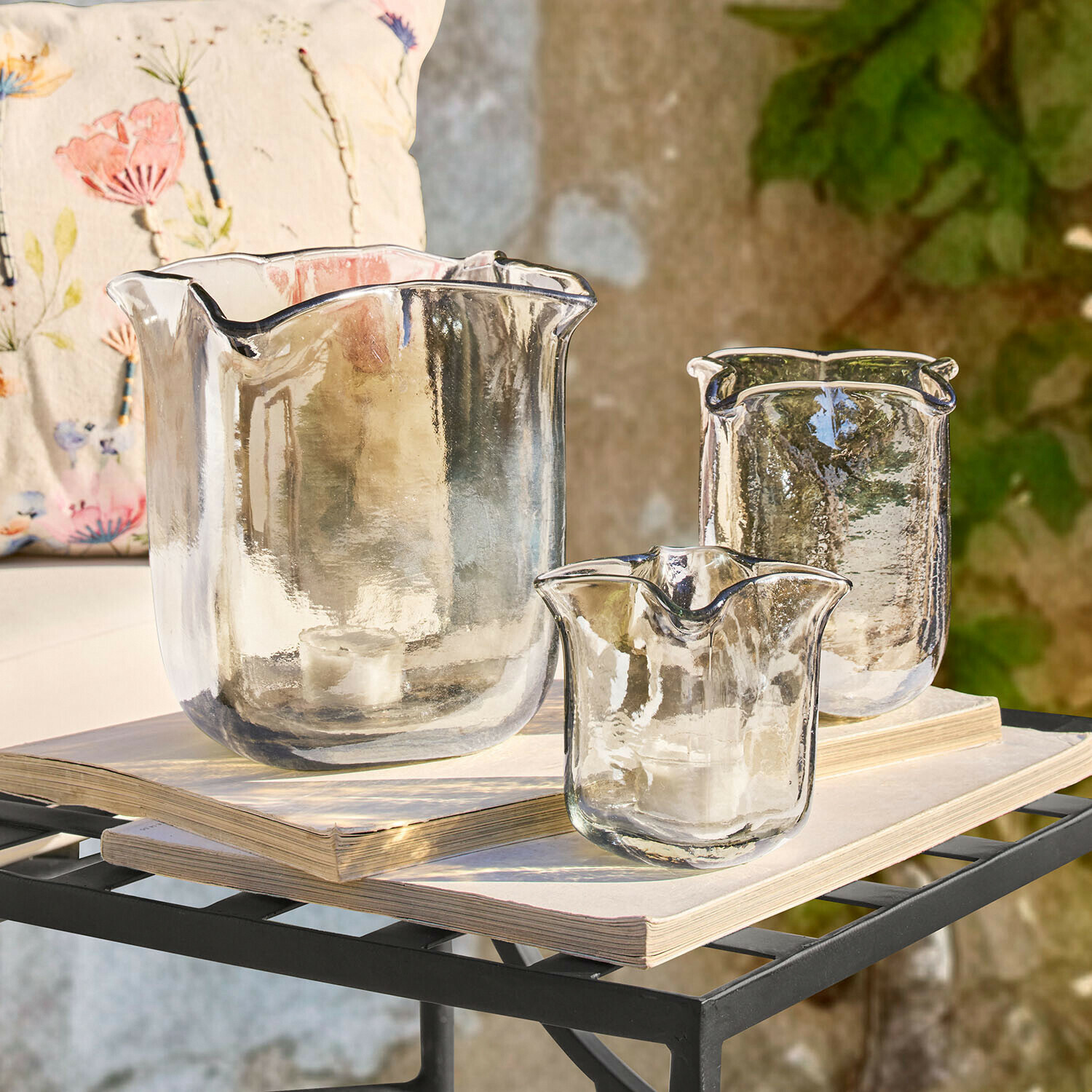 Zestaw trzech przezroczystych szklanych świeczników o nieregularnym kształcie na książkach