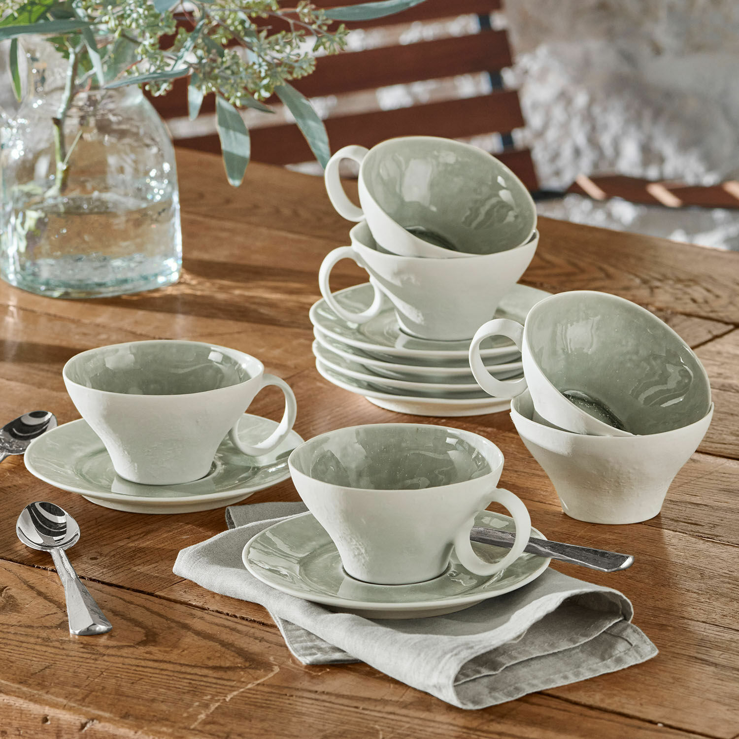 Zestaw filiżanek i spodków 6 szt. Braganza Zestaw białych ceramicznych filiżanek z zielonym wnętrzem na drewnianym stole z łyżeczkami