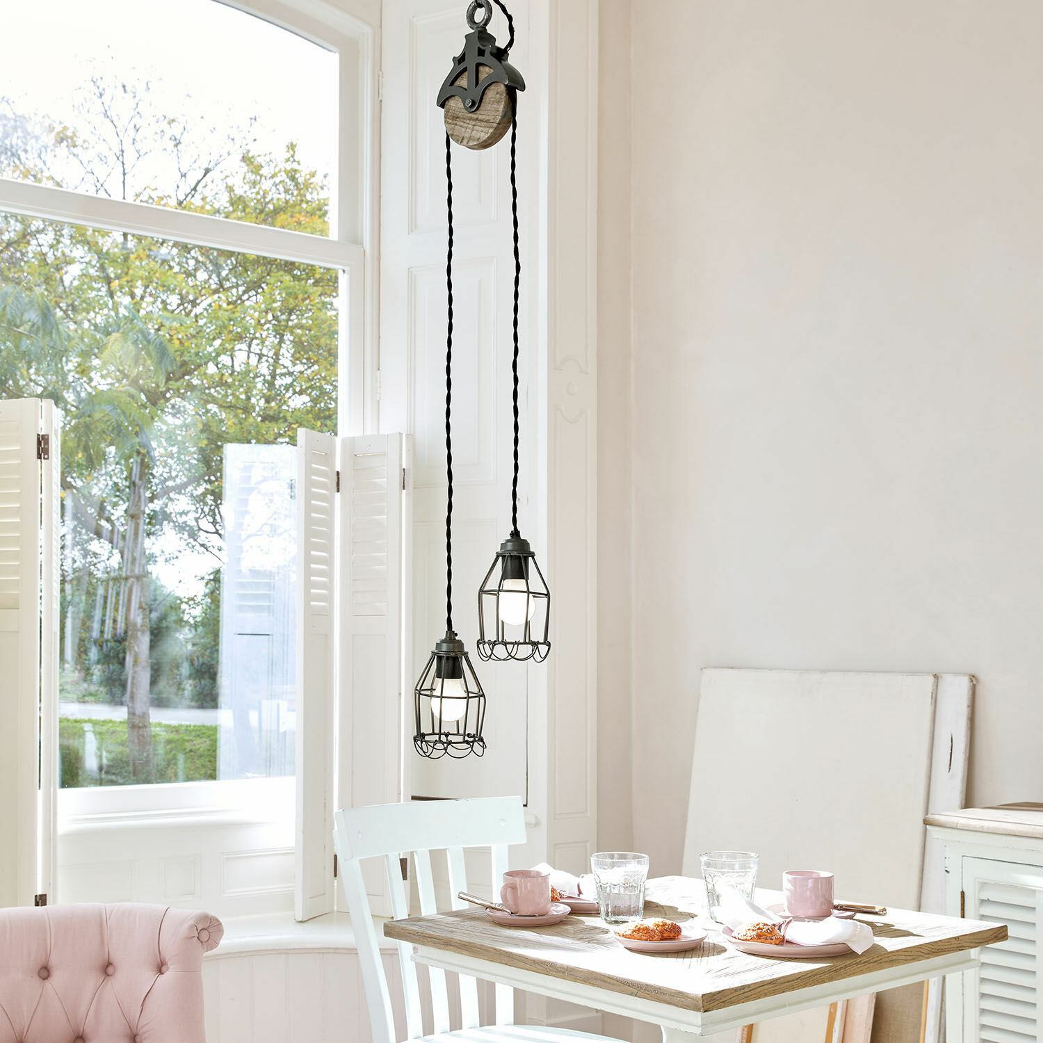 Lampa wisząca Trevici Dwa czarne metalowe lampy wiszące z klatką ochronną nad drewnianym stołem w jasnym wnętrzu