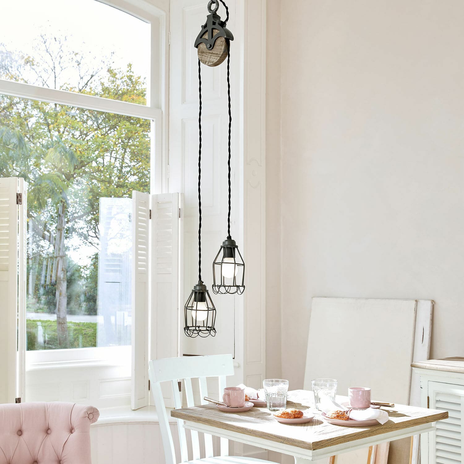 Lampa wisząca Trevici Dwa czarne metalowe lampy wiszące z klatką ochronną nad drewnianym stołem w jasnym wnętrzu