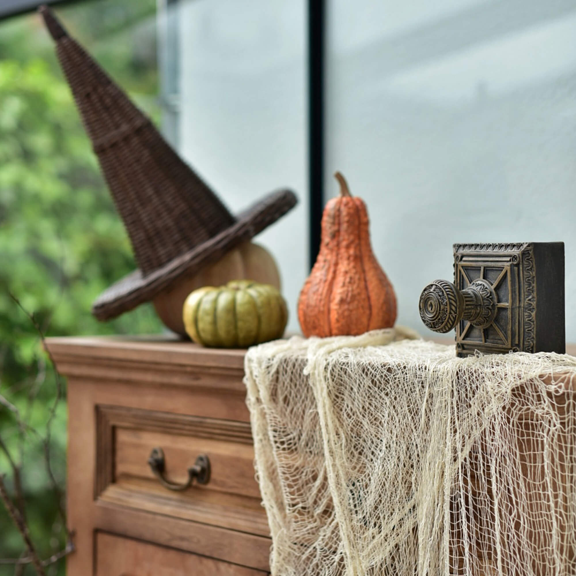 Dekoracyjna drewniana komoda z wiklinowym kapeluszem czarownicy i dyniami na Halloween
